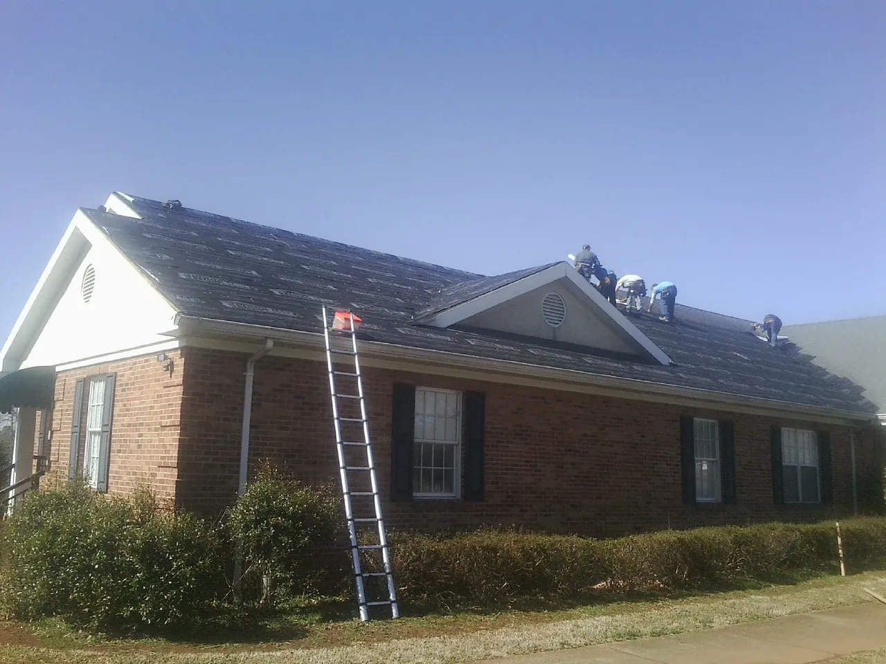 Crew tearing shingles off a brick ranch roof with a ladder set — Emergency Roof Repair work by our crew in Niota