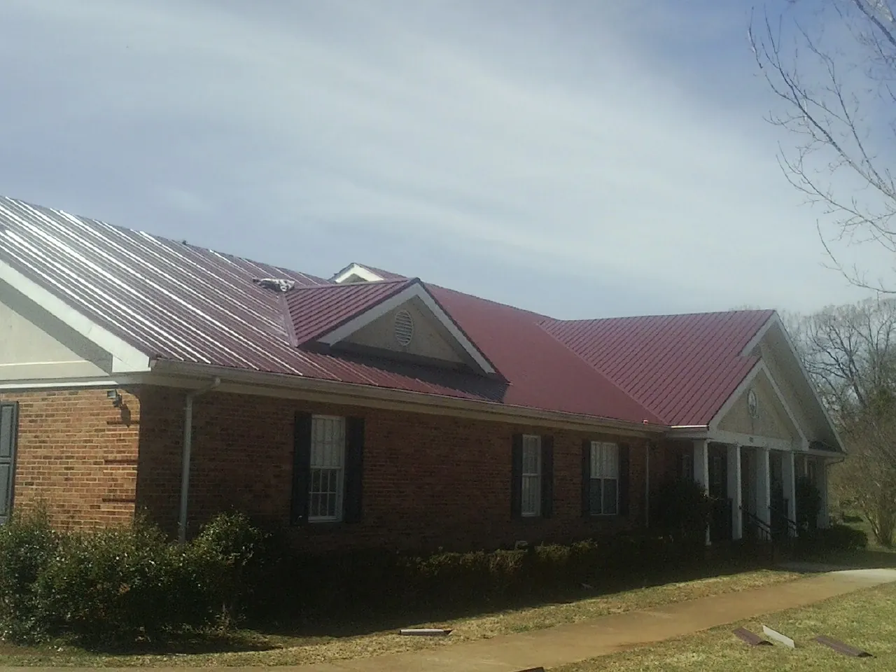 Red metal roof with gabled entries on a long brick building, from a Hail Damage Roof Repair job in Niota