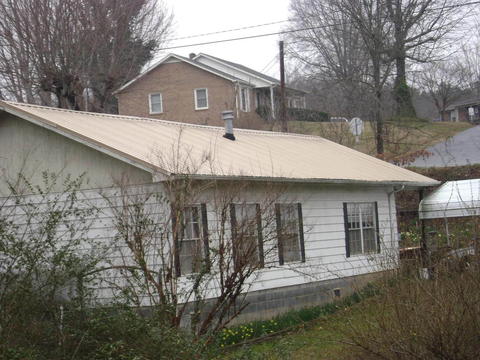 Tan metal roof on a white sided house set into a hillside — Commercial Roofing by Roofing Brothers in Niota
