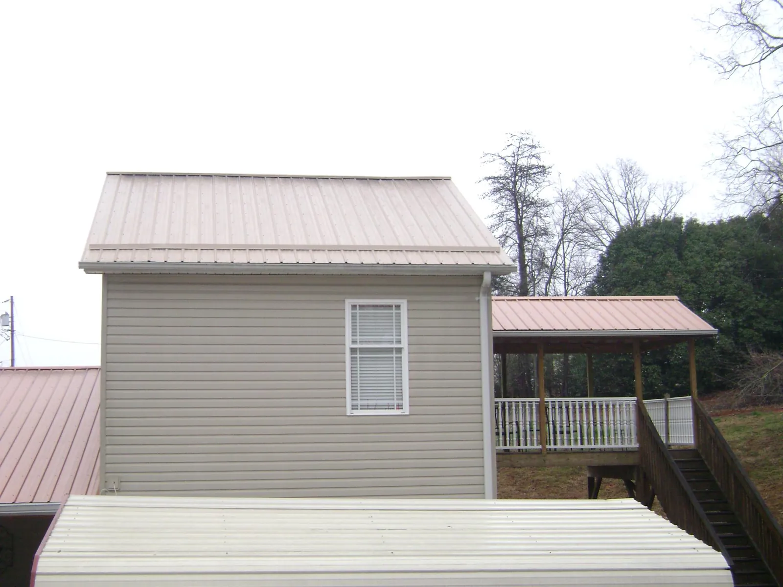 Tan metal roofs on a two story addition and attached porch, from a Roof Replacement job in Niota